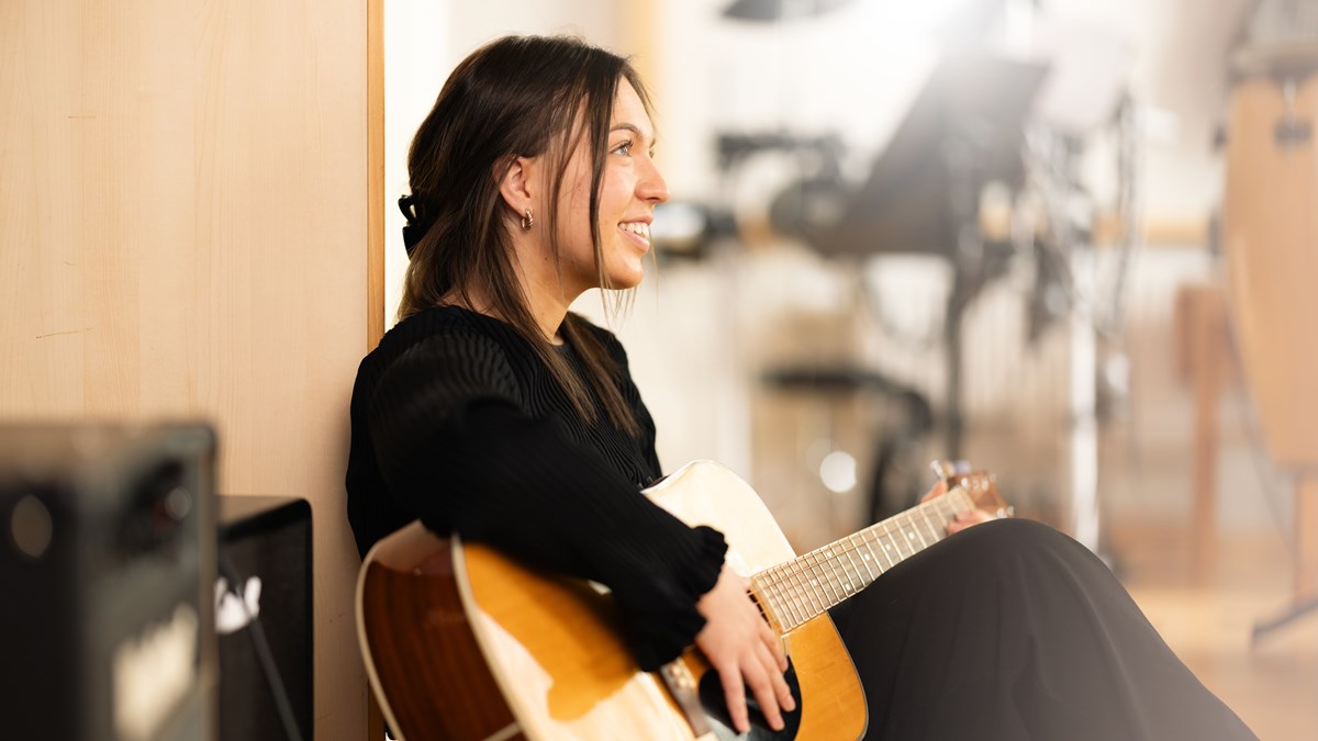 Leende tjej som sitter med en gitarr